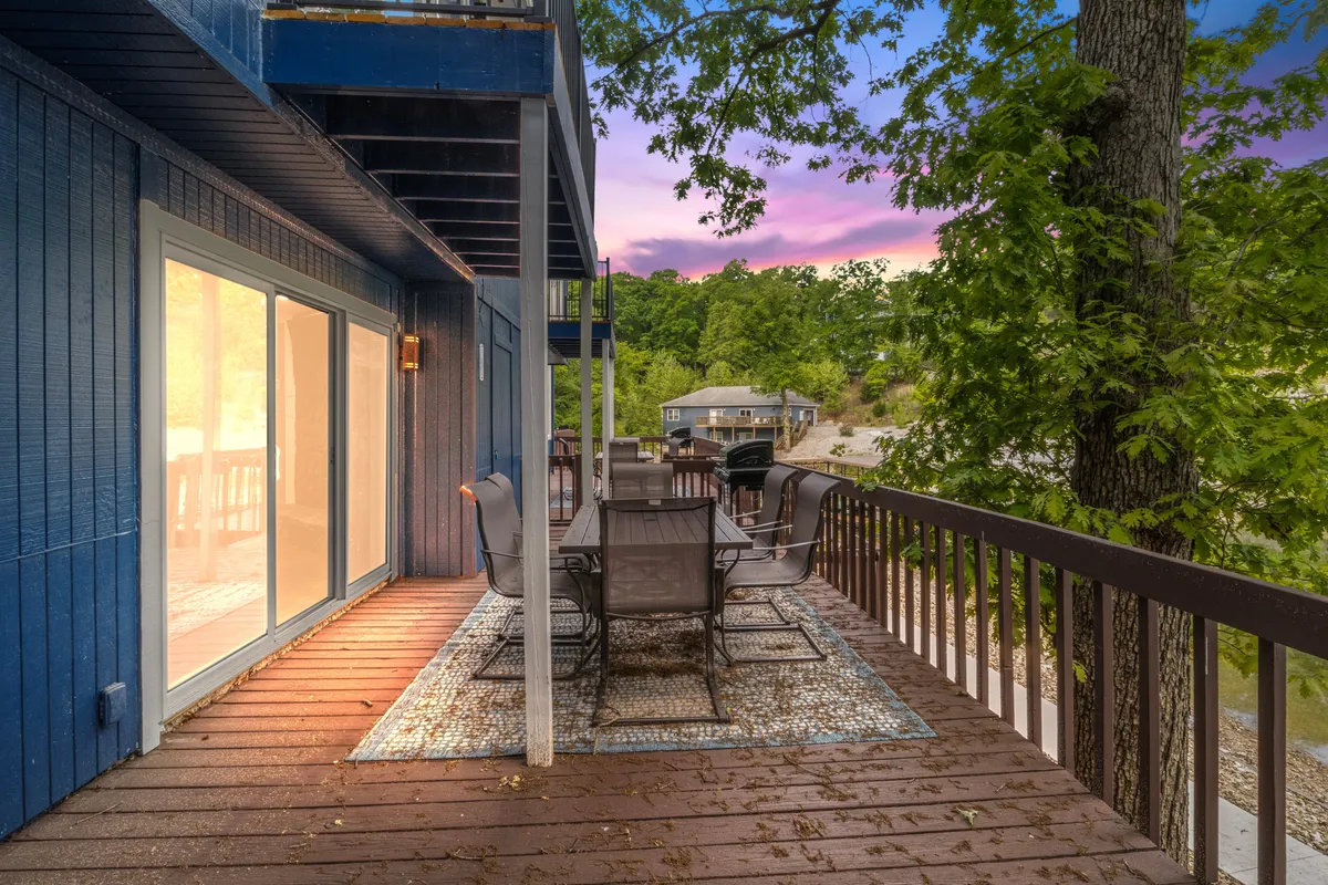 An exterior shot of the deck featuring a dining table surrounded by greenery, with sliding glass doors that connect directly to the living area, perfect for outdoor meals or relaxing after a day by the lake.