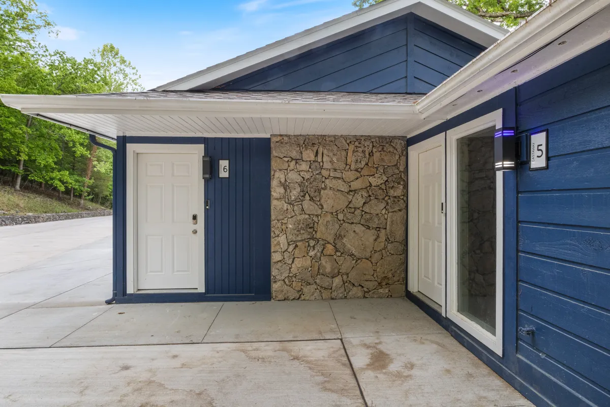 A welcoming exterior shot of the property, featuring blue wooden siding, a stone wall, and white doors, suggesting both inviting curb appeal and access to local attractions.