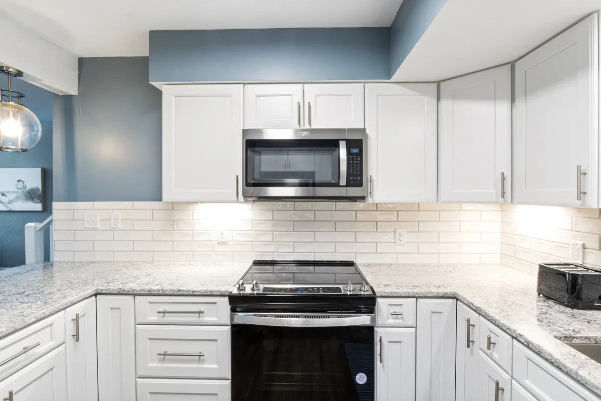 This image showcases a welcoming kitchen space with a granite countertop, stainless steel appliances, white cabinetry, and a subway tile backsplash. The area exudes functionality and warmth, designed for gathering and preparing meals together.