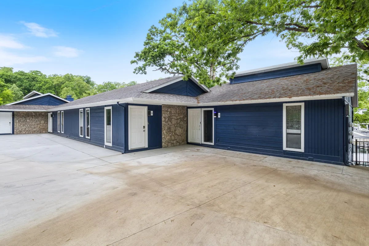 A welcoming view of the blue exterior, featuring a large driveway where children can play, surrounded by trees and greenery. The image conveys a sense of space and the familial atmosphere of the retreat, with possibilities for outdoor gatherings or celebrations.